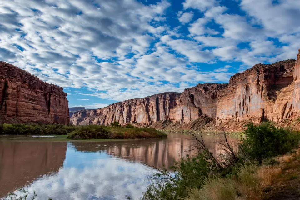 View of Colorado River winding through canyon in red rock cliffs against lightly cloudy blue sky
